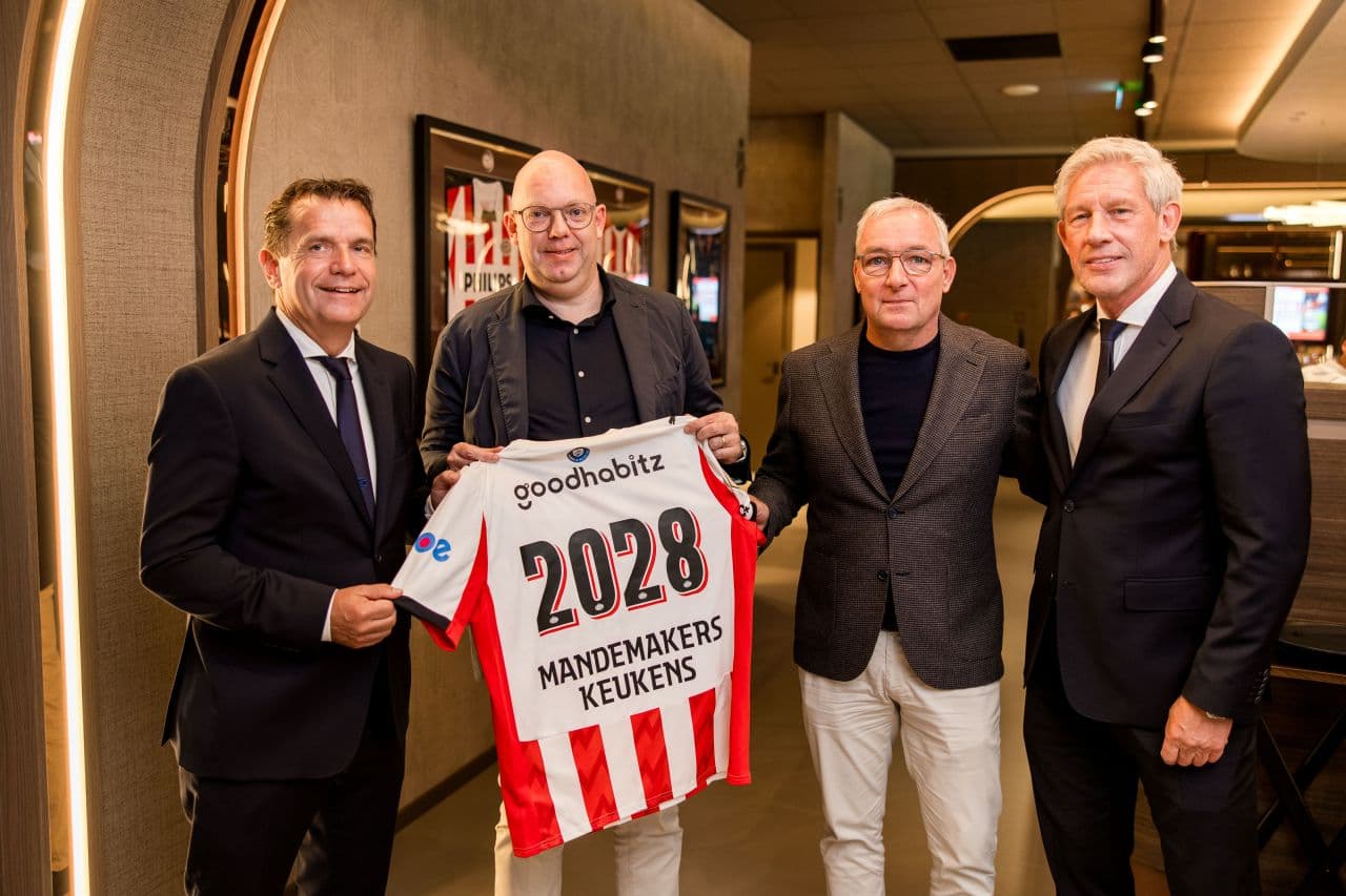 Foto van vier mannen op een rij waarbij een man een PSV shirt vasthoudt