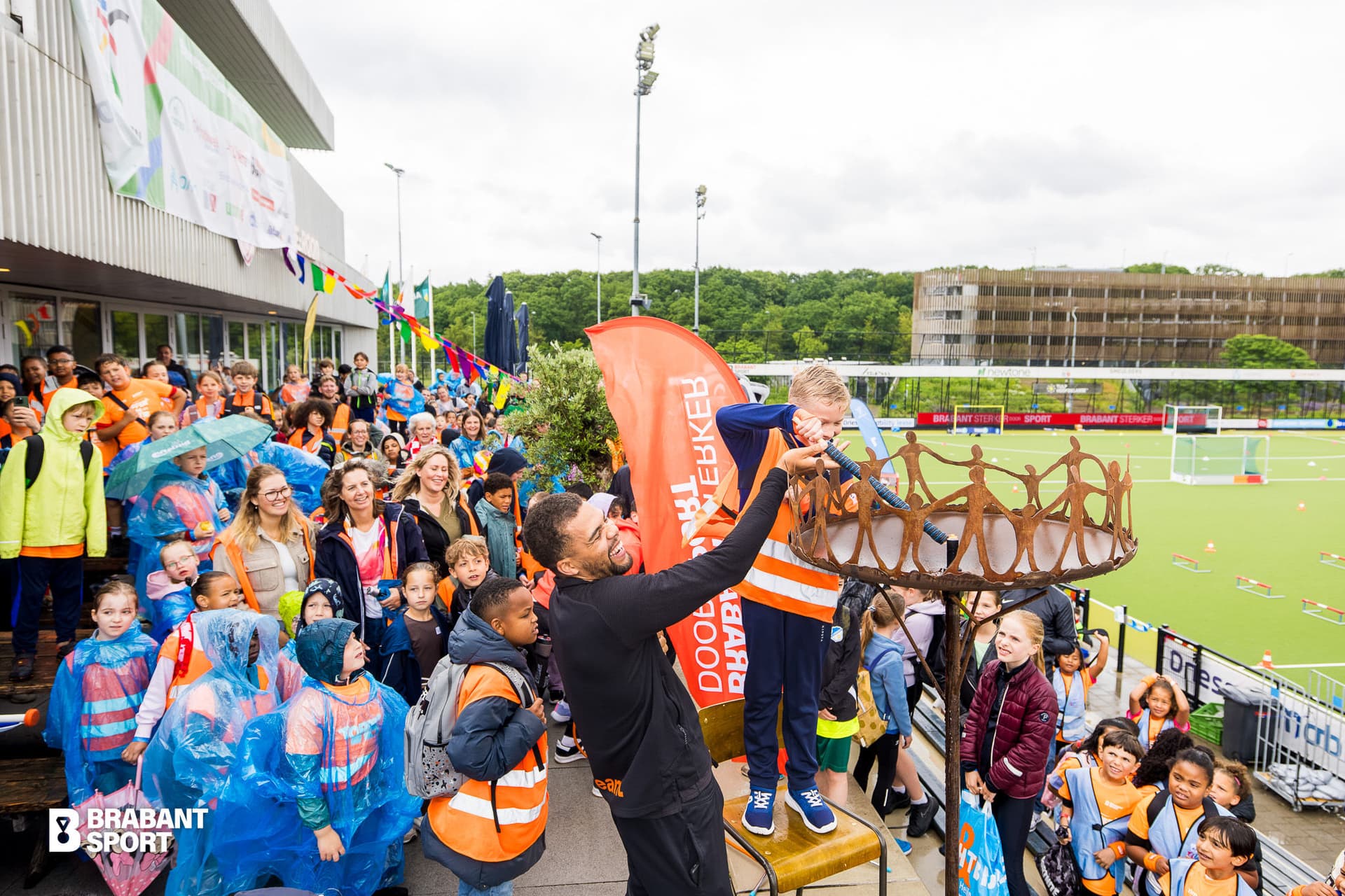 20260604_BrabantSport_DeSpelen-064-4257.jpg Foto waar een jongetje met hulp van een volwassen man het Olympisch kinderspelen vuur aansteekt